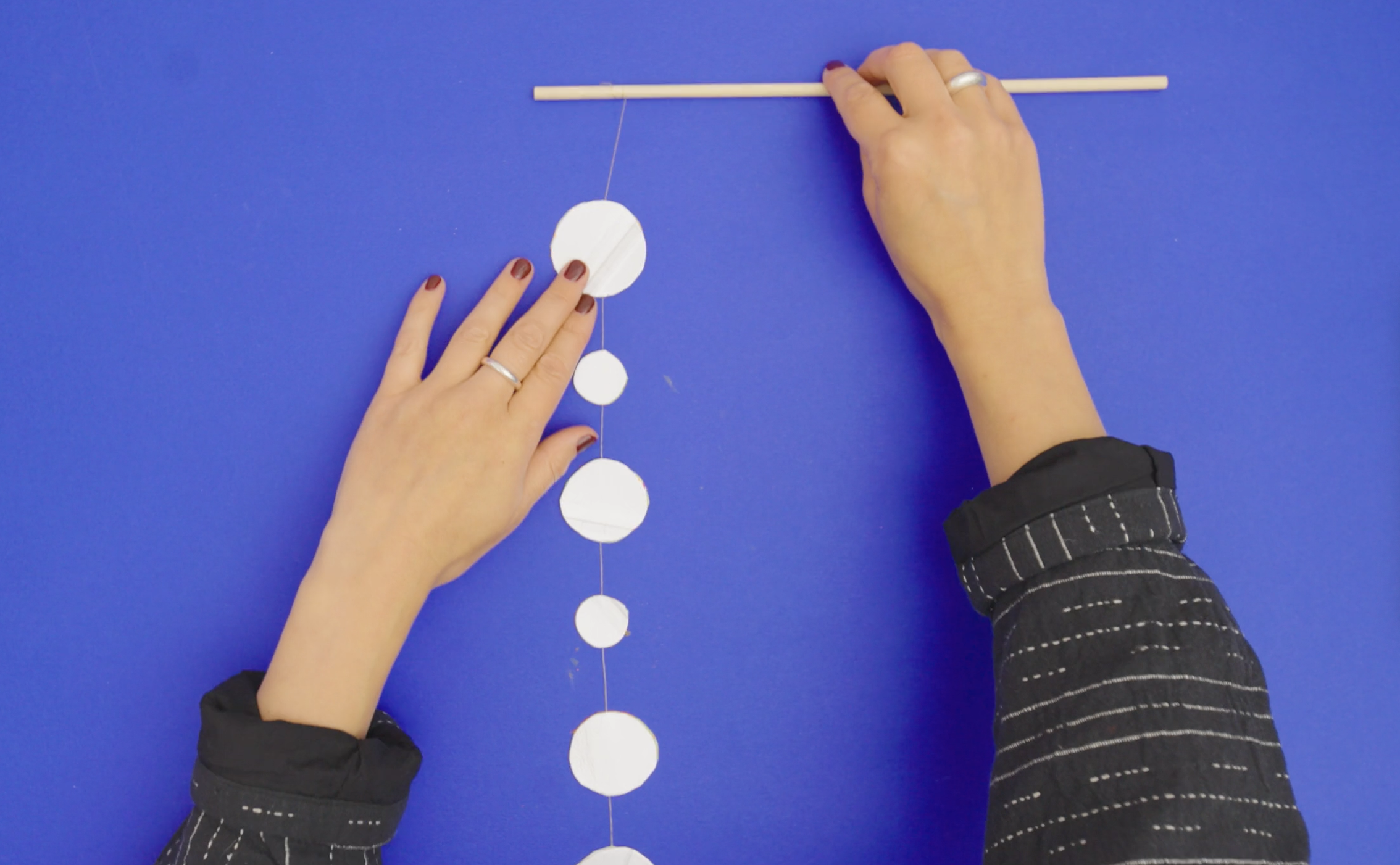 hands make a hanging sculpture against a blue background, threading circles onto a thread